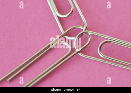 Three joined paper clips on pink background - Concept of unity and solidairity between women Stock Photo