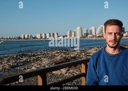 a handsome man drinking Yerba Mate Infusion in the rambla of Punta del Este, Maldonado, Uruguay with the atlantic ocean and city at the background Stock Photo