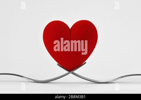 Two forks holding a heart on white background - Concept of love Stock Photo
