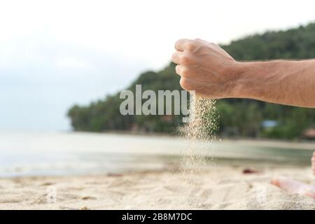 Play with sand on the beach. Sand is poured from the hands, against the backdrop of a tropical island Stock Photo