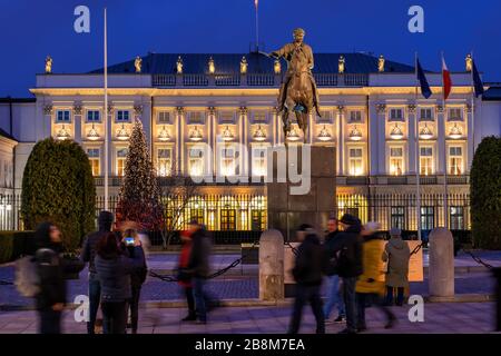 Warsaw, Poland - December 27, 2019: People at the Presidential Palace illuminated at night and Monument to Prince Jozef Poniatowski, city landmarks Stock Photo