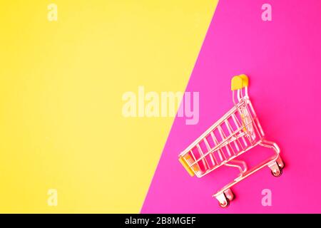 Empty stainless steel shopping cart isolated on pink and yellow background with copy space for your text or design. Top view, flat lay of shopping tro Stock Photo