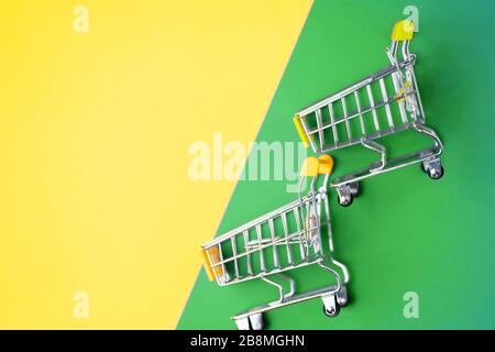 Supermarket, mall, market, shopping, sale concept. Two empty miniature toy trolley on yellow and green background, copy space for text or design. Flat Stock Photo