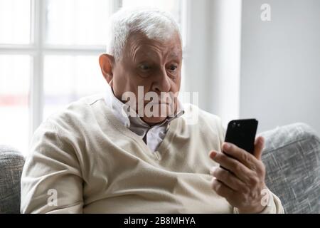 Old man holding smartphone look at device screen feels amazed Stock Photo