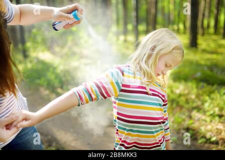 Mother applying insect repellent to her daughter before forest hike beautiful summer day. Protecting children from biting insects at summer. Using bug Stock Photo