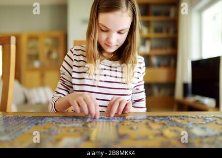 Cute young girl playing puzzles at home. Child connecting jigsaw puzzle pieces in a living room table. Kid assembling a jigsaw puzzle. Fun family leis Stock Photo