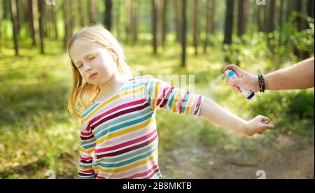 Mother applying insect repellent to her daughter before forest hike beautiful summer day. Protecting children from biting insects at summer. Using bug Stock Photo