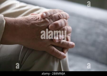 Old man sitting on couch palms folded on knee closeup Stock Photo