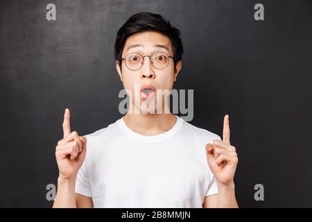 Close-up portrait of amused and excited happy asian man visit amusement park for first time, pointing fingers up at something super cool, say wow Stock Photo