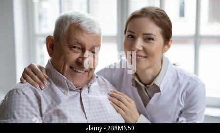 Caring nurse hugs old man patient smiling looking at camera Stock Photo