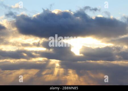 The sun at sunset or dawn behind the clouds, shines through. The sun's rays in the sky. Stock Photo