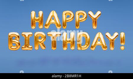 Words HAPPY BIRTHDAY made of golden inflatable balloons floating on blue background. Gold foil helium balloons forming phrase. Birthday Stock Photo