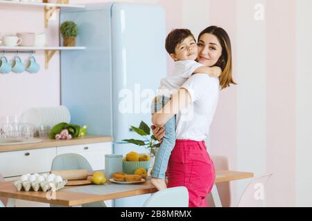Beautiful mother and little son are hugging in the kitchen, happy time and togetherness Stock Photo