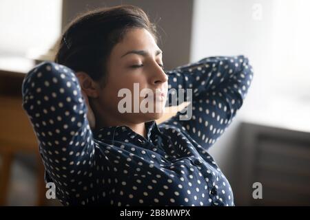 Close up peaceful young Indian woman relaxing, stretching on chair Stock Photo