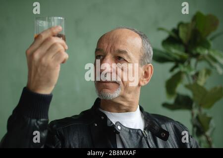 Senior man with beard and mustache holds glass of brandy or whisky. Alchol degustation, tasting concept Stock Photo