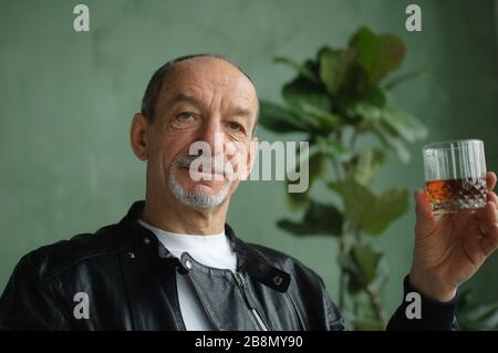Close-up of mature man holding glass with whiskey near his face and looking at camera, senior male portrait Stock Photo