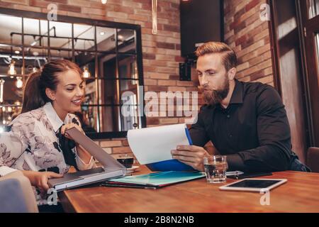 Young business people working together on paper work and talking about reports and finance. Portrait of young business man and woman sitting in cafe a Stock Photo