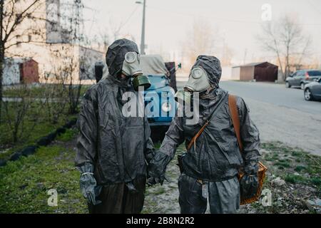 Couple in love holds hands in NBC protective suits and gas masks. Concept of a preventive measures and protection for coronavirus COVID 19 pandemic an Stock Photo