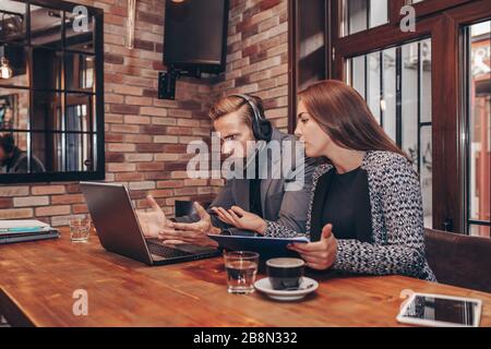 Two worried employees reading bad news together on line in a laptop  comparing documents .Man and woman working together on paper work and talking abo Stock Photo