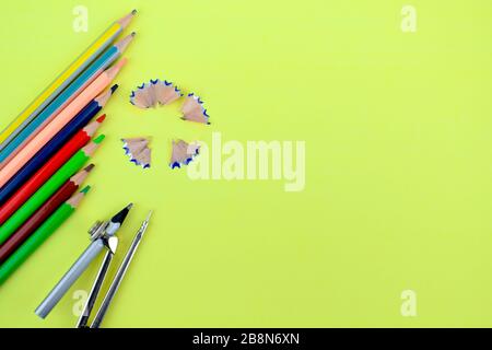 Different colored wood pencils and a pencil attached to a pencil compass pointing at a pencil shaving on a yellow background Stock Photo