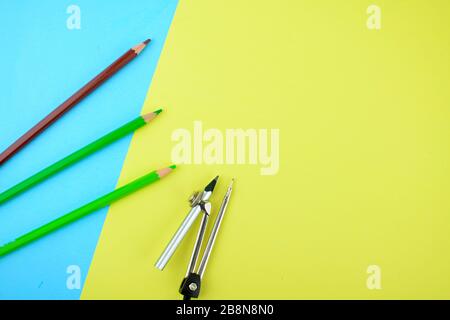 Some different colored pencil crayons and a silver pencil attached to a pencil compass scattered on a paper background Stock Photo