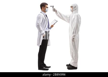 Full length profile shot of a man in a hazmat suit measuring body temperature to a male doctor wearing medical mask isolated on white background Stock Photo