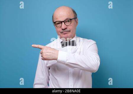 Confident senior man point away. Serious mature male gesturing with finger aside Stock Photo
