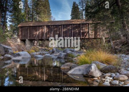 A view of  Yosemite Wawona covered Bridge over the Merced  River by Mariposa, in the fall, featuring yellow colors, and blue sky California, USA