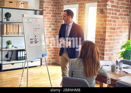 Two middle age business workers smiling happy and confidentt working together with smile on face. Man standing doing work presentation using board and Stock Photo