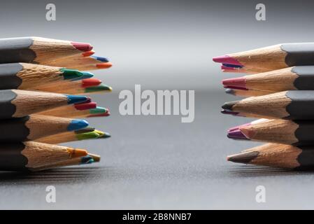 A closeup image of two opposing sets of coloured pencils on a grey background with copyspace in the centre Stock Photo