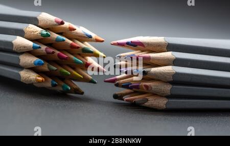 A closeup image of two opposing sets of coloured pencils on a grey background Stock Photo