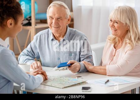 Travel agent at office sitting with senior clients man givving passport and money smiling happy Stock Photo
