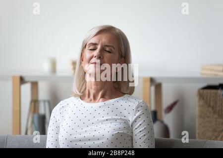 Peaceful middle aged blonde woman relaxing with closed eyes. Stock Photo