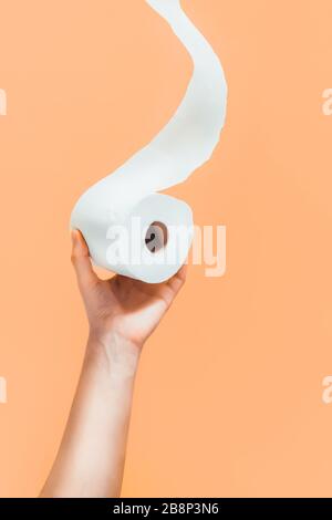 Close up caucasian male hand pulling or holding a roll of toilet paper from buttom on light orange, beige background. Crisis product lack concept. Mod Stock Photo