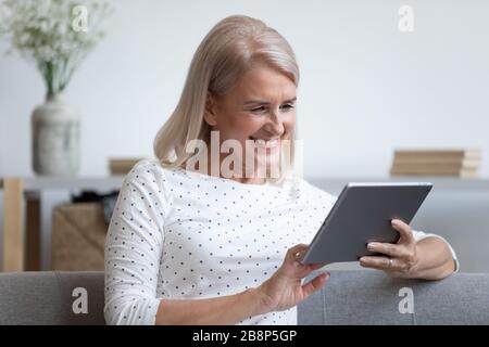 Happy older lady holding computer tablet in hands. Stock Photo