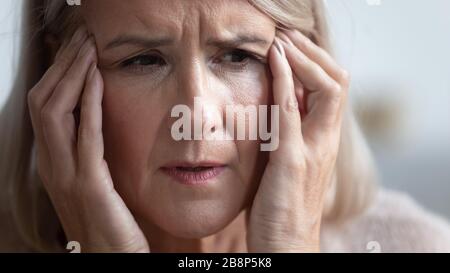 Unhealthy mature retired woman suffering from strong sudden headache. Stock Photo