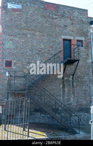 a close up view of a metal stair case leading up to a solid black door on the side of a building Stock Photo