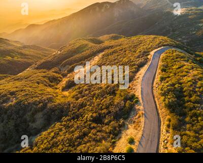 Aerial view of a winding road along the edge of a green lake surrounded ...