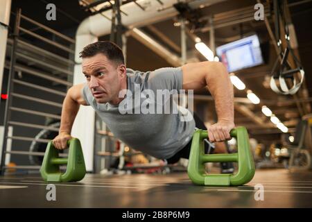Full length portrait of mature muscular man doing push ups on stand during strength workout in modern gym, copy space Stock Photo