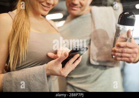 Close up of smiling couple using smartphone during workout in gym, focus on female hand in foreground, copy space Stock Photo