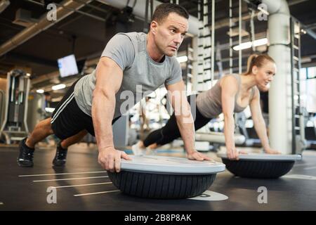 Full length portrait of mature muscular man doing balance exercises during couple workout in modern gym, copy space Stock Photo