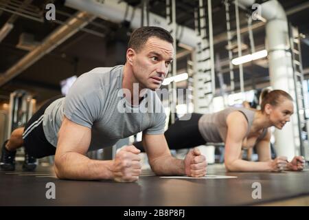 Full length portrait of mature muscular man doing plank exercises during couple workout in modern gym, copy space Stock Photo
