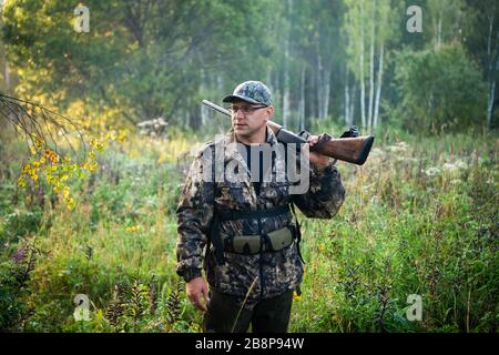 Silhouette of a hunter on the background of the morning red dawn. Stands at the ready with a gun. Stock Photo