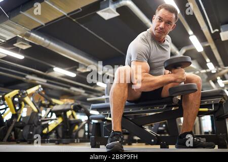 Low angle portrait of mature muscular man doing exercises with dumbbells during strength workout in modern gym, copy space Stock Photo