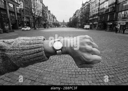 Almost desolate Wenceslas Square (Václavské náměstí) in Prague, Czech Republic, pictured at 1.17 p.m. during the COVID-19 coronavirus pandemic quarantine (lockdown) on 19 March 2020. The photograph is homage to the famous photograph by Czechoslovak photographer Josef Koudelka pictured at the same place during the Soviet invasion to Czechoslovakia in August 1968. The handless watch on the left hand of the photographer actually is an entrance chip to the Šutka Aquacentrum which is useless during the quarantine because all swimming pools are also closed indefinitely due the corona virus outbreak. Stock Photo