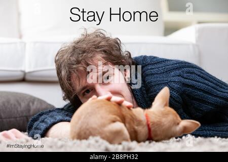young man staying at home in a living room playing with his puppy far away from corona virus COVID19 infection out there Stock Photo