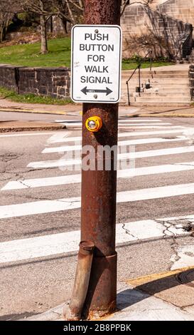 A push button box and sign for a crosswalk with the crosswalk in the background at an intersection Stock Photo