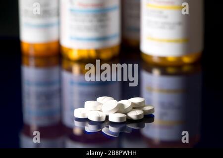 White tablets on dark reflective surface with prescription bottles in background.