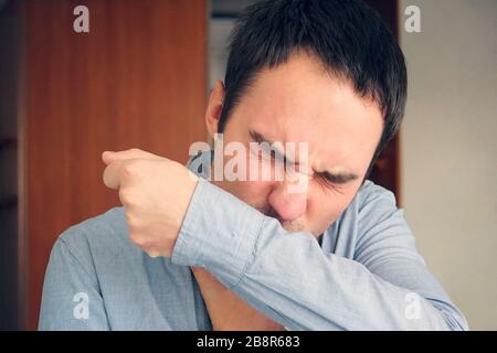 man having the flu and sneezing on her sleeve in the crook of her arm. A young guy coughs into the fabric of his shirt to prevent the spread of viral Stock Photo