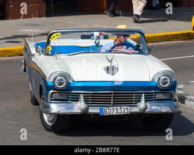 Cuban wearing hat driving a blue classic Ford car. Vintage cars are all around the city of Havana, Cuba, also know as La Habana. Stock Photo